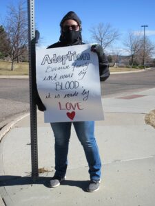 Department of Human services staffer holds a sign: Adoption - Because family isn't made by BLOOD, it is made by LOVE.